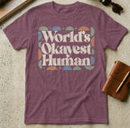 Burgundy t-shirt with "World's Okayest Human" text in colorful geometric shapes.