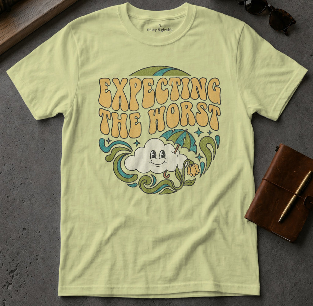 Light yellow t-shirt with "EXPECTING THE WORST" text and cartoon cloud.