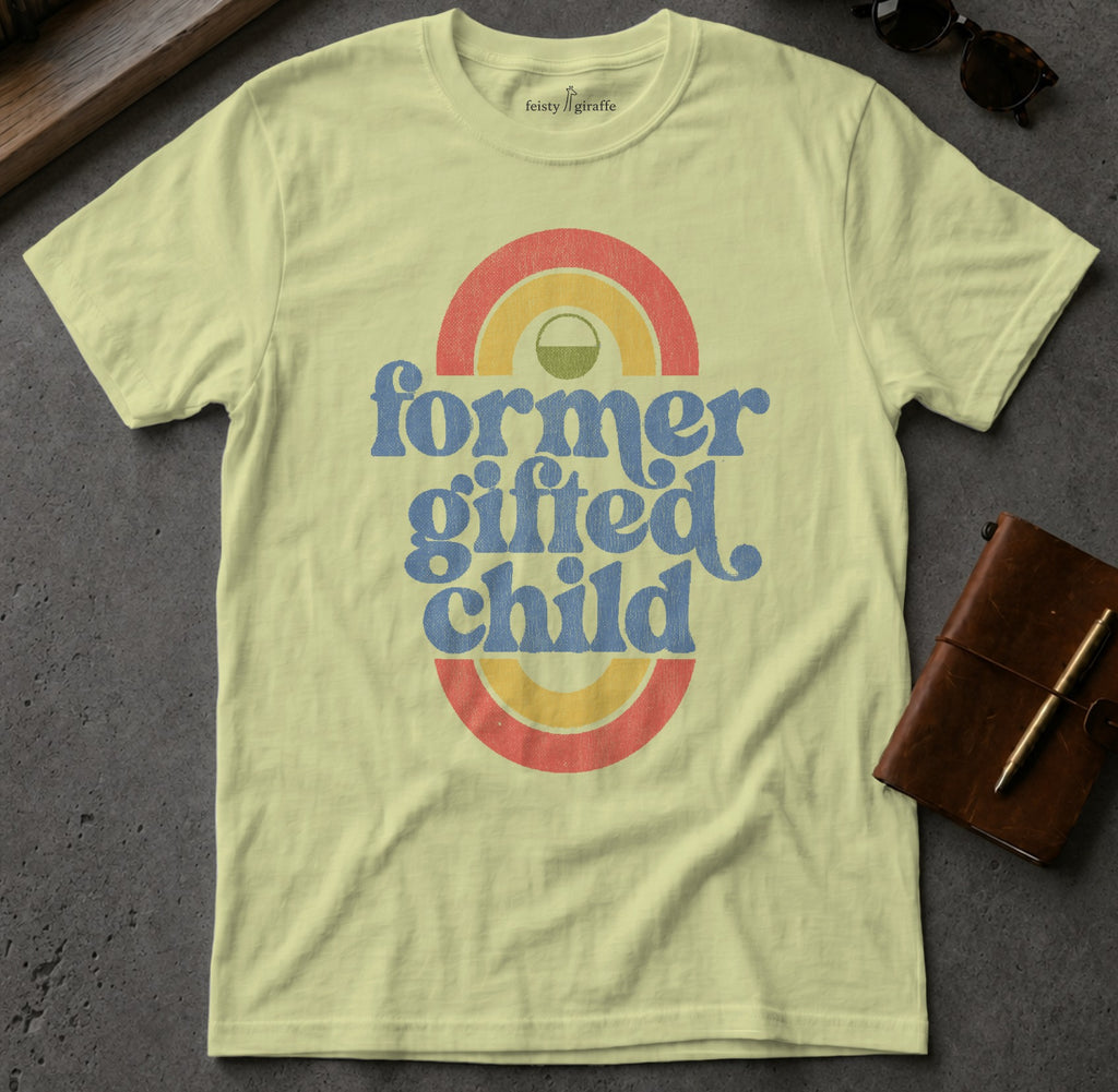 "Former gifted child" text on a pale yellow t-shirt with rainbow graphic.