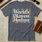 Dark grey t-shirt with "World's Okayest Human" text in retro colorful font.