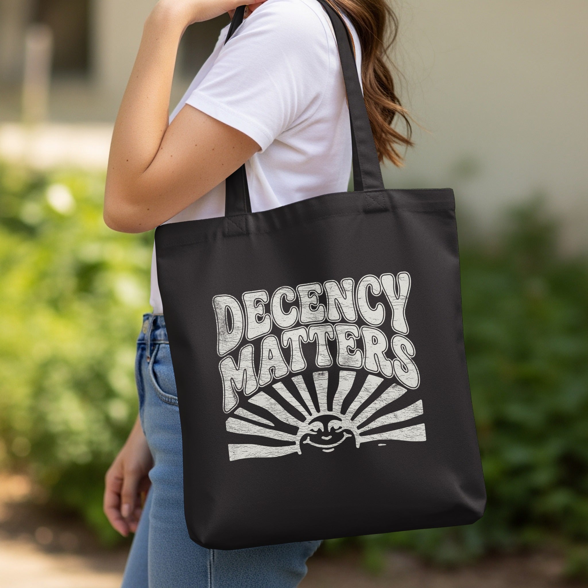 Decency Matters Smiling Sun Rays Black Tote Bag product type
Tote bag, Decency Matters, Smiling sun, Sun rays, Black bag, White print, Shopping bag, Carryall bag, Reusable bag, Statement bag, Positive message, Retro design, Graphic tote, Kindness bag, Respect message, Ethics support, Morals advocacy, Unique design, Social justice, Activist bag