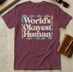 Burgundy t-shirt with "World's Okayest Human" text and geometric pattern.