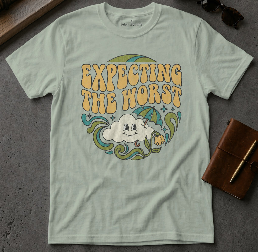 Light blue t-shirt with "Expecting the worst" text and smiling cloud graphic.