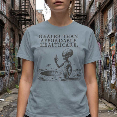 Gray t-shirt with alien in crater and text "REALER THAN AFFORDABLE HEALTHCARE."